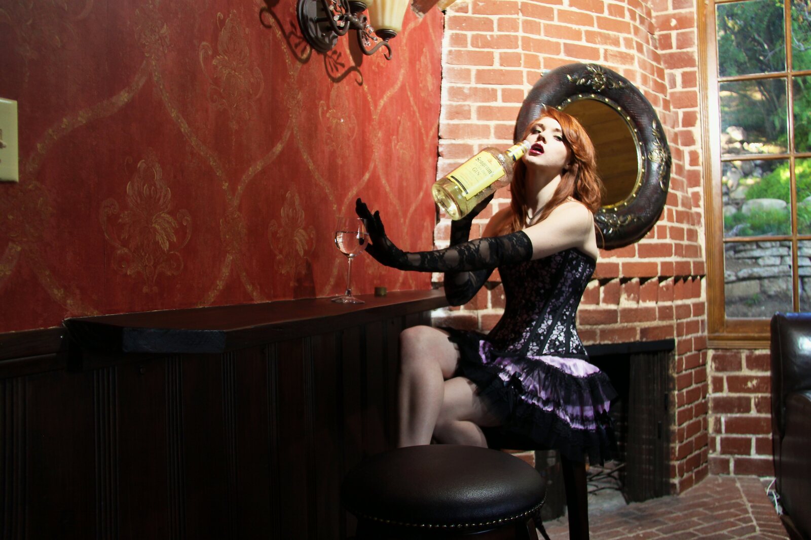 Model in a corset dress at a dark bar against red wallpaper and brick
